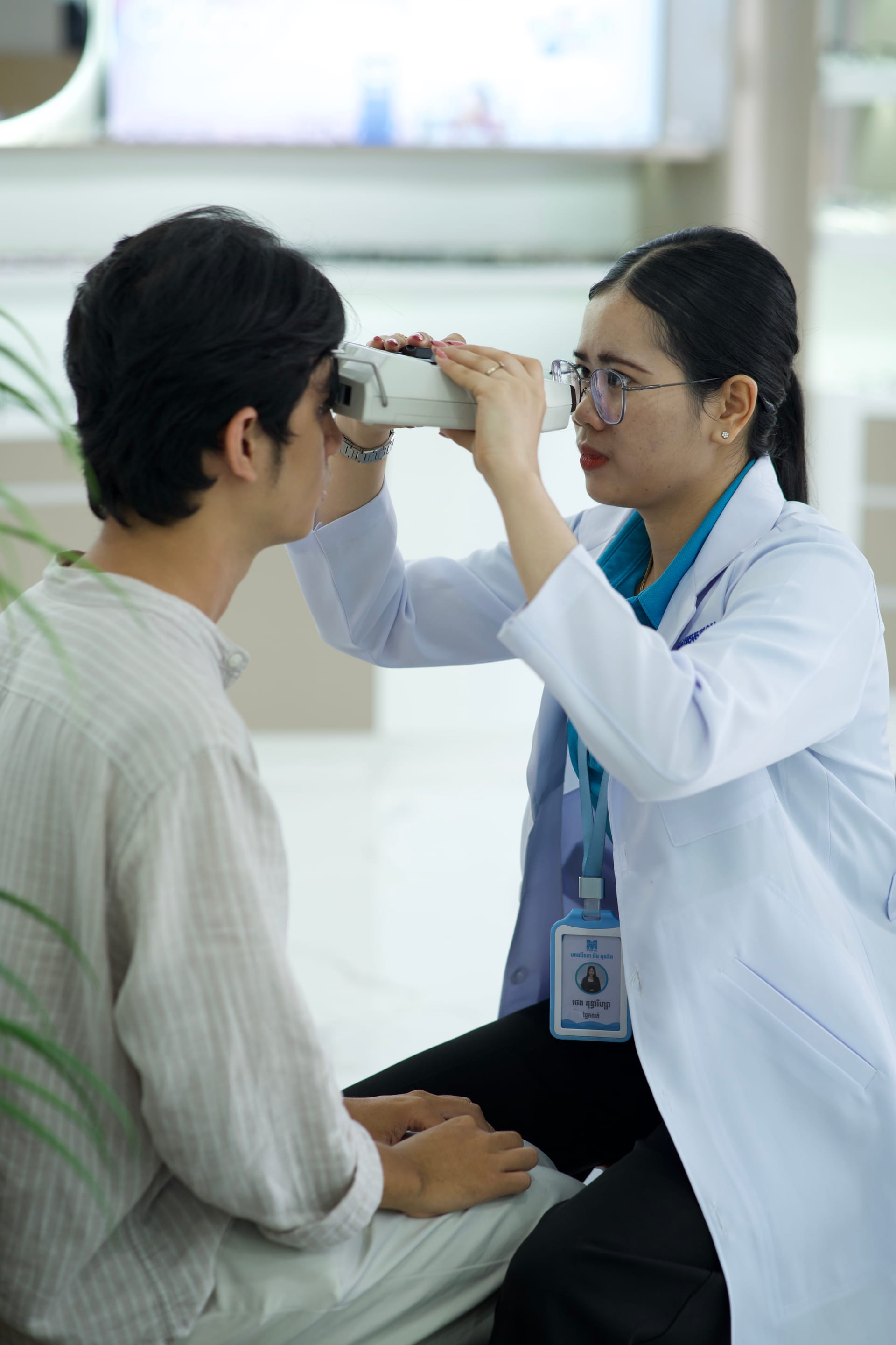 Licensed M-Optic optician measuring pupillary distance and adjusting custom eyeglass frame fit for customer in Phnom Penh
